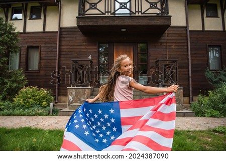 Happy girl with american flag running on lawn near vacation house