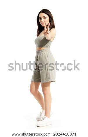 Happy young beautiful woman in summer clothes showing two fingers victory hand sign. Full body portrait isolated on white background