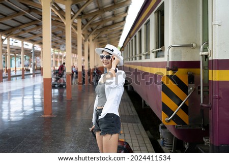 Asian woman with suitcase waiting for train at railway station.