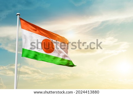 Niger national flag waving in beautiful clouds.