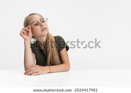 Pensive, thoughtful. Portrait of one teen blonde caucasian girl in casual clothes and glasses isolated over white studio background. Copyspace for ad.