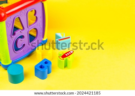 Children's background. Educational toy sorter in the form of a cube with bright figures on a yellow background. Development of fine motor skills and thinking of the baby. Space for the text.