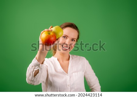 A beautiful middle-aged woman in a white shirt shows apples on a green background. The concept of diet, healthy food, vegetarianism.