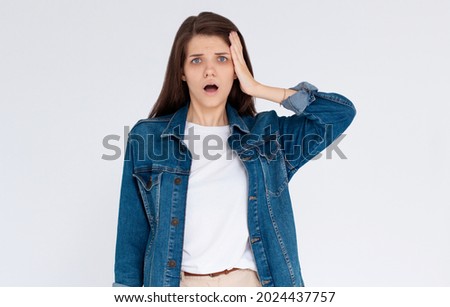 Horrible, stress, shock. Female half-length portrait isolated at blue studio. Young emotional surprised woman clasping head in hand. Human emotions, facial expression concept.