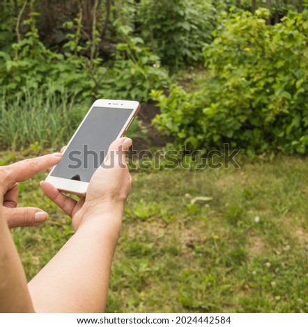 Close-up of a woman's hand using a smartphone to send a message against the background of green grass in the garden in summer.