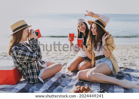 Full size three friends fun young women in straw hat summer clothes have picnic hang out take photo drink liguor glasses raise toasts outdoors on sea beach background People vacation journey concept