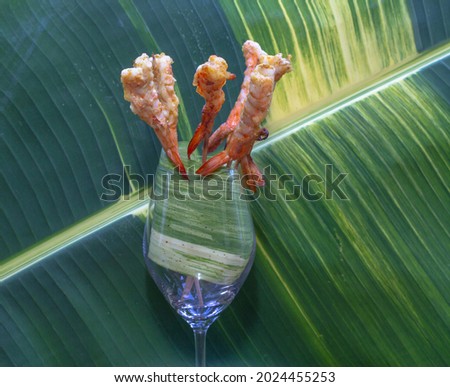 Grilled shrimp on skewers placed in a glass of wine 
with speckled banana leaves in the background.
beautiful color of nature background. food and restaurant concept.
