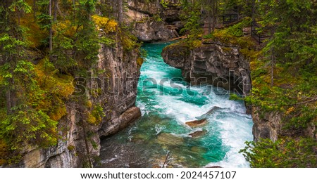 Maligne Canyon Alberta Canada in summer showing beautiful Canyon with rocks covered with green moss, orange lichens, green forest and beautiful turquoise green glacial water streaming through Royalty-Free Stock Photo #2024457107