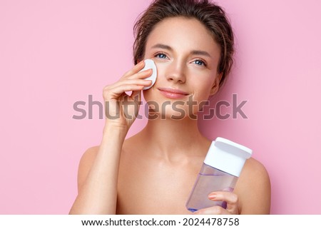 Woman removing makeup, holds cotton pads near face. Photo of woman with perfect skin on pink background. Beauty and skin care concept