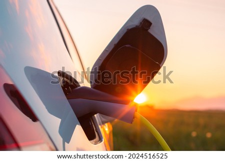 Close up shot of an opened electric car charging socket cap and charger plugged into, at a public electric charging station near the highway at sunset Royalty-Free Stock Photo #2024516525