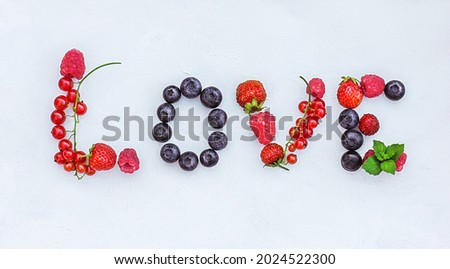 Top view of various berries on a light gray background. The letters of the word LOVE