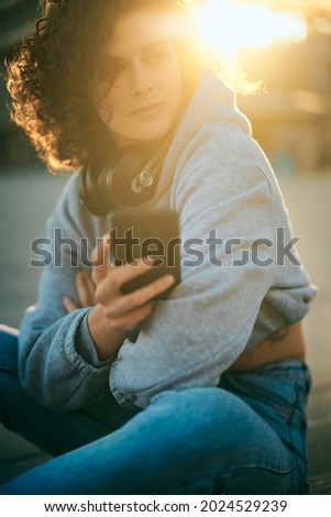 Young woman with curly hair sitting on the street and chilling.
