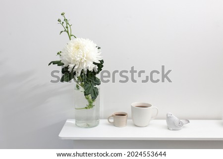 A large chrysanthemum in a glass vase, two fluted cups of coffee and ceramic bird figurines on the table. Office decoration. Copy space