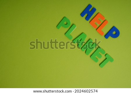 A closeup of a colorful writing on a green background that reads "help planet"- climate change concept