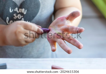 The baby draws with wax crayon on his hand
