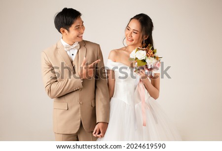Young attractive Asian couple, man wearing beige suit, woman wearing white wedding gown standing together holding hands. Concept for pre wedding photography. Royalty-Free Stock Photo #2024619590