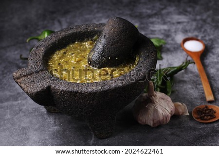 Mexican green sauce in molcajete. Green chili peppers, garlic, green tomato, onion, two wooden spoons and coriander on dark gray background. Royalty-Free Stock Photo #2024622461