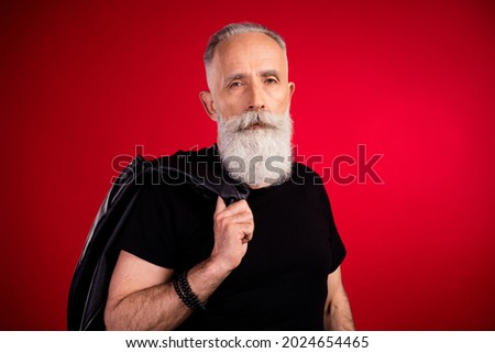 Portrait of attractive serious fashionable grey-haired man holding leather jacket good look isolated over bright red color background
