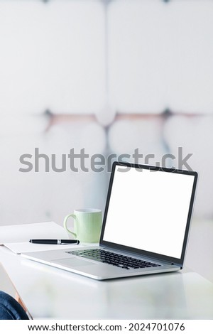 Mockup blank screen laptop computer with pen and notebook on white top table, vertical view.