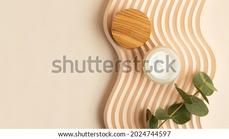 Open skin care packaging with white cream inside.Wooden cover near it. Box lying on the wavy podium.Pastel colors,good as mockup,large banner.