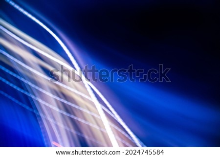 Abstract colorful background with  white and blue glowing lines of different thickness and curvature from city lights on a black background. The blur is intentional.