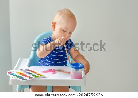 Happy cheerful child drawing with brush in album using a lot of painting tools. Creativity concept.
