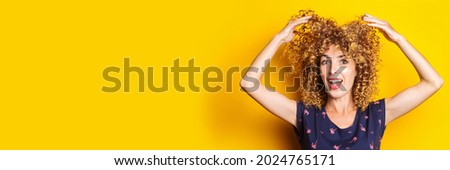 cheerful curly young woman lifts her hair up on a yellow background. Banner