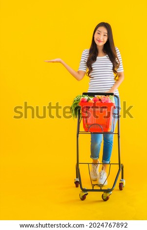 Portrait beautiful young asian woman shopping grocery from supermarket and cart on yellow isolated background