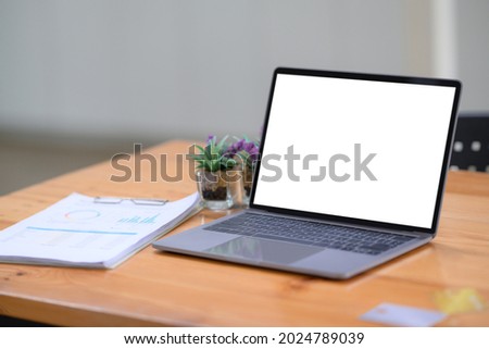 Computer laptop and documents on wooden table in office.