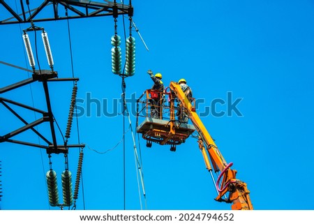 High voltage power line transmission tower workers with crane and blue sky. Hydro linemen on boom lifts working on high voltage power line towers. Royalty-Free Stock Photo #2024794652
