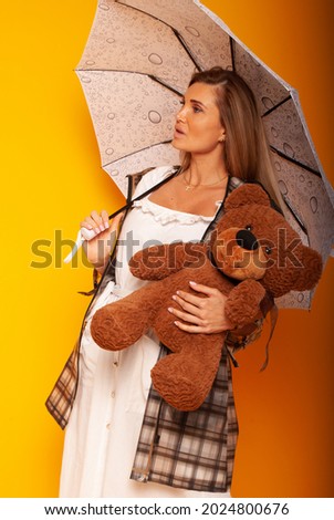 Girl under an umbrella on a yellow background, rainy weather, Teacher is late for school. A girl holding a bear in her arms