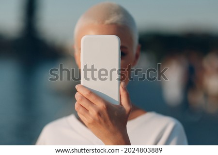 Short haired woman covering close face with smartphone. Mobile phone data security, privacy and confidentiality concept. Royalty-Free Stock Photo #2024803889