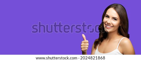 Photo of woman showing thumb up hand sign or like gesture, isolated on violet purple color background. Portrait of happy smiling gesturing brunette girl at studio. Wide horizontal banner composition