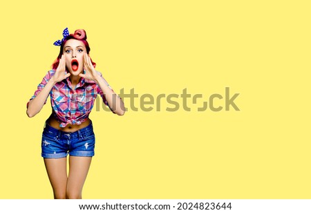 Portrait of woman holding her hands near opened mouth and saying or shout something. Pin up girl. Red purple haired model in retro vintage studio concept, over yellow color. Copy space mock up.