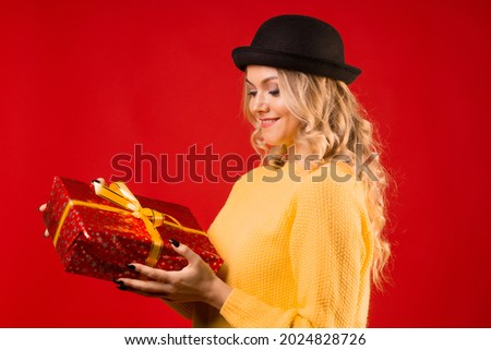 Winter holiday, a young woman in knitted clothes and a bowler hat, holding a gift box with a ribbon