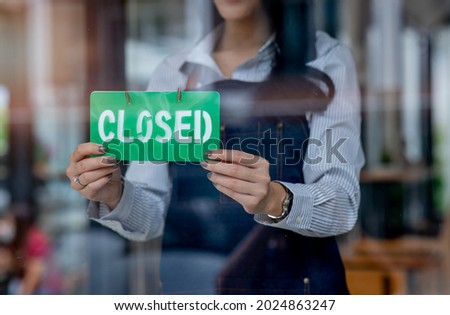 Caucasian female turning sign from open to closed on the entrance door of his small cafe. Out of business