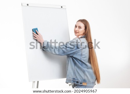 Young woman student in denim clothes wipes with sponge white board isolated on white background. Education concept