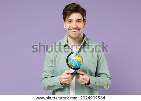 Young fun smiling excited happy caucasian man 20s wearing casual mint shirt white t-shirt hold in hands Earth world globe isolated on purple violet background studio portrait People lifestyle concept.