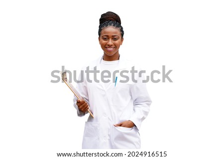 Beautiful young black doctor or scientist stands against a white background wearing a white lab coat and holding a clipboard with braided hair, smiling                                Royalty-Free Stock Photo #2024916515