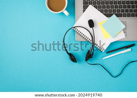 Top view photo of laptop headset with microphone cup of coffee pens copybook and sticker notes on isolated pastel blue background with copyspace