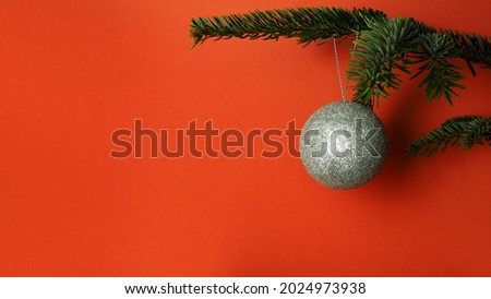 on the right, a gray round ball hangs on a branch of a green Christmas tree on a red background . side view . Christmas. copy space