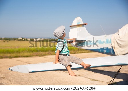 A baby boy is sitting on the wing of a sports plane.