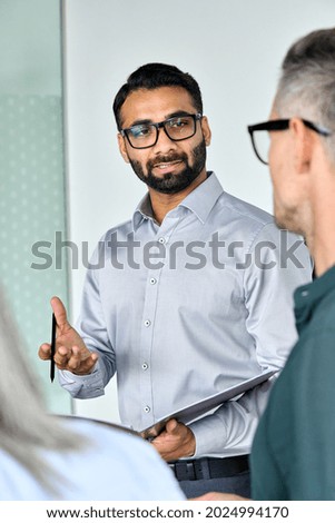 Diverse executive business team group listening to Indian executive ceo holding contract discussing project standing at boardroom meeting. Multiracial team doing paperwork in office. Vertical. Royalty-Free Stock Photo #2024994170