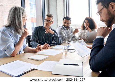 Diverse international executive business partners group discuss report at boardroom meeting table. Multiracial team negotiating project developing business strategy doing paperwork analysis in office. Royalty-Free Stock Photo #2024994257