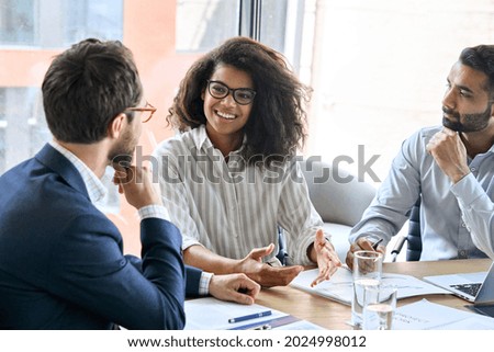 Smiling female manager talking to businessmen team discussing financial sales research plan at boardroom meeting table. Multiethnic team working together developing business strategy in modern office. Royalty-Free Stock Photo #2024998012