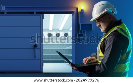 Refrigerator in warehouse. Freezer is built into warehouse. Warehouse worker near freezer. Storage worker with laptop. Refrigeration equipment. Concept - Refrigerator for products on storage. Royalty-Free Stock Photo #2024999296