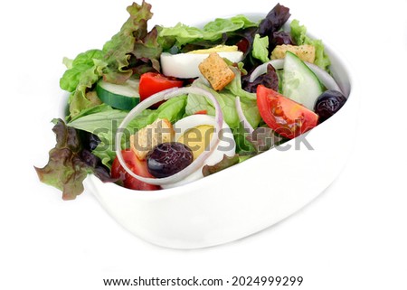A bowl of mixed salad greens, tomato, onions, hard boiled eggs, olives, croutons and cucumbers. Image on white with copy space.