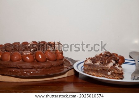 Slice of chocolate cake on a white plate, next to a chocolate cake on a wooden football stand with a slice missing