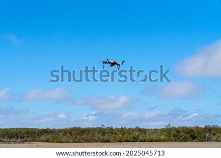 A drone flying above mangrove salt pans against a cloudy blue sky, ready to take aerial photographs of the landscape
