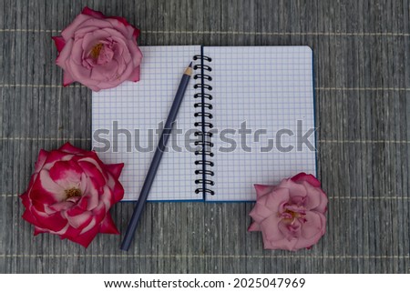 On a light background lies a notebook, roses and a pencil.